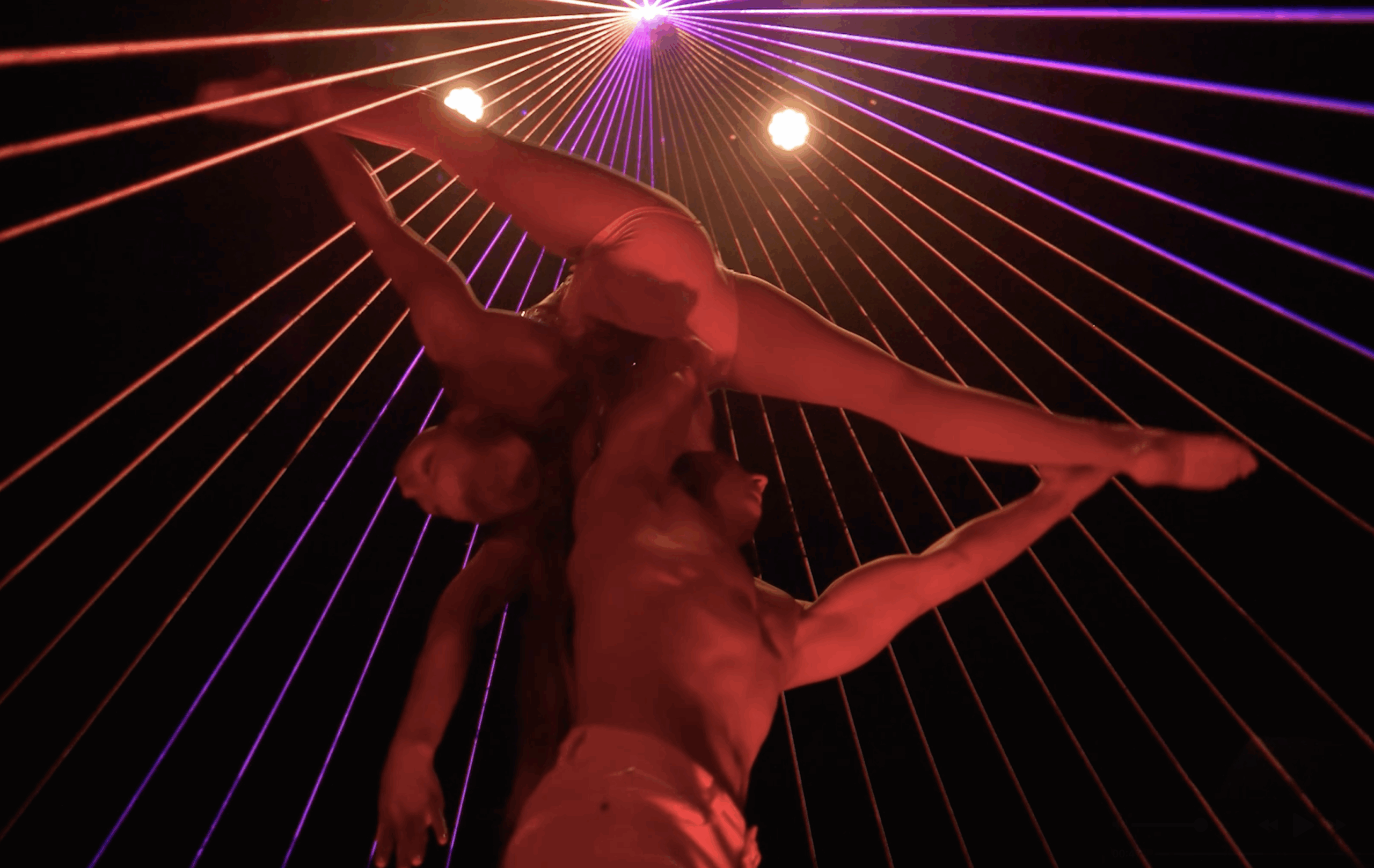 Laser Dance Show .Zwei Akrobaten führen auf der Bühne eine dramatische Hebefigur vor, die von roten und violetten Laserstrahlen beleuchtet wird, die in einer dunklen Umgebung über den Kopf strahlen.