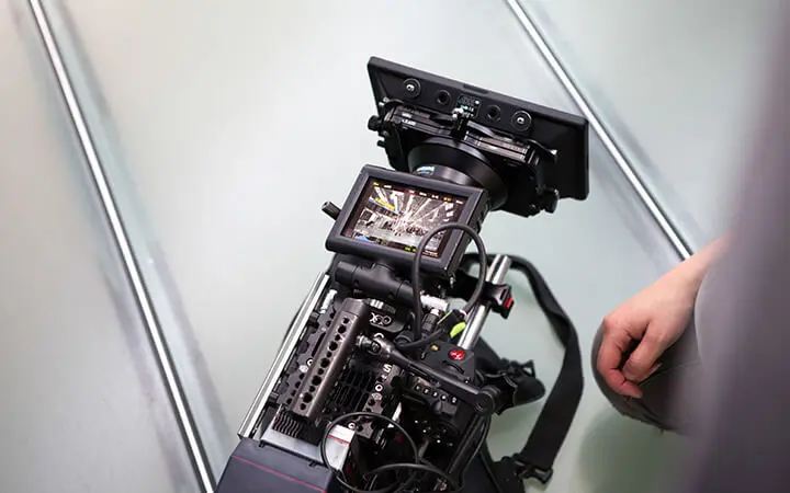 Eine Nahaufnahme einer professionellen Videokamera, die auf einem Stativ mit mehreren Bildschirmen und Kabeln aufgebaut ist - perfekt für einen Freestyler, der dynamische Aufnahmen macht. Auf der rechten Seite des Bildes ist die Hand einer Person zu sehen.