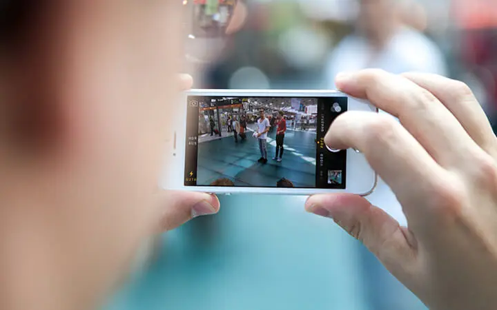 Ein Freestyler fotografiert mit seinem Smartphone eine Gruppe von Menschen, die in einem gut beleuchteten, öffentlichen Raum stehen. Auf dem Bildschirm des Telefons ist deutlich die lebendige Szene zu sehen, die fotografiert wird.