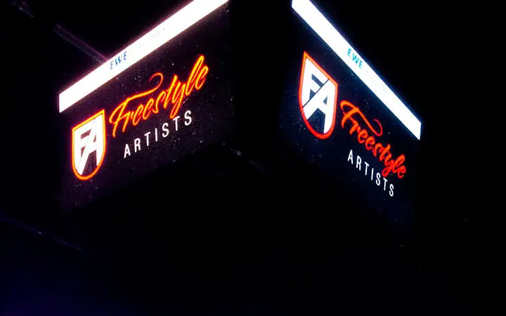 Zwei große digitale Schilder zeigen das Logo von Freestyle Artists mit einem stilisierten FA-Schild und dem Schriftzug Freestyle Artists in Orange und Weiß vor einem dunklen Hintergrund, um ihre Präsenz in der Unterhaltungsbranche zu unterstreichen.