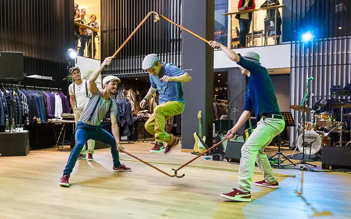 Vier Männer führen im Supertalent einen traditionellen ungarischen Stocktanz auf, bei dem ein Mann springt, während er zwei Stöcke in einer Rautenform hält, während die anderen Stöcke halten; im Hintergrund sind Kleiderständer und ein Schlagzeug zu sehen.