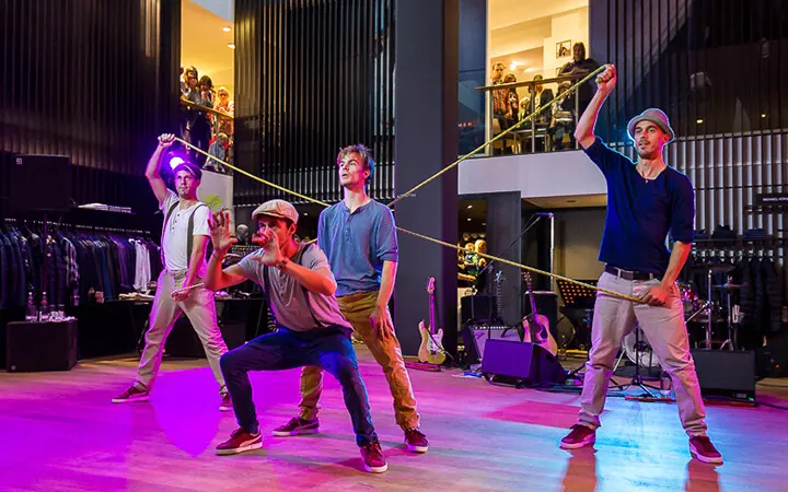 Vier Männer treten auf einer Bühne auf, zwei halten ein langes gelbes Seil, die anderen posieren dynamisch darunter und fesseln das Supertalent-Publikum, das von einem Balkon in einer modernen Halle zusieht.